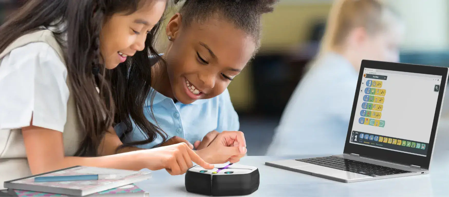 Two girls engaging with the Root coding robot and laptop, experiencing interactive coding education.