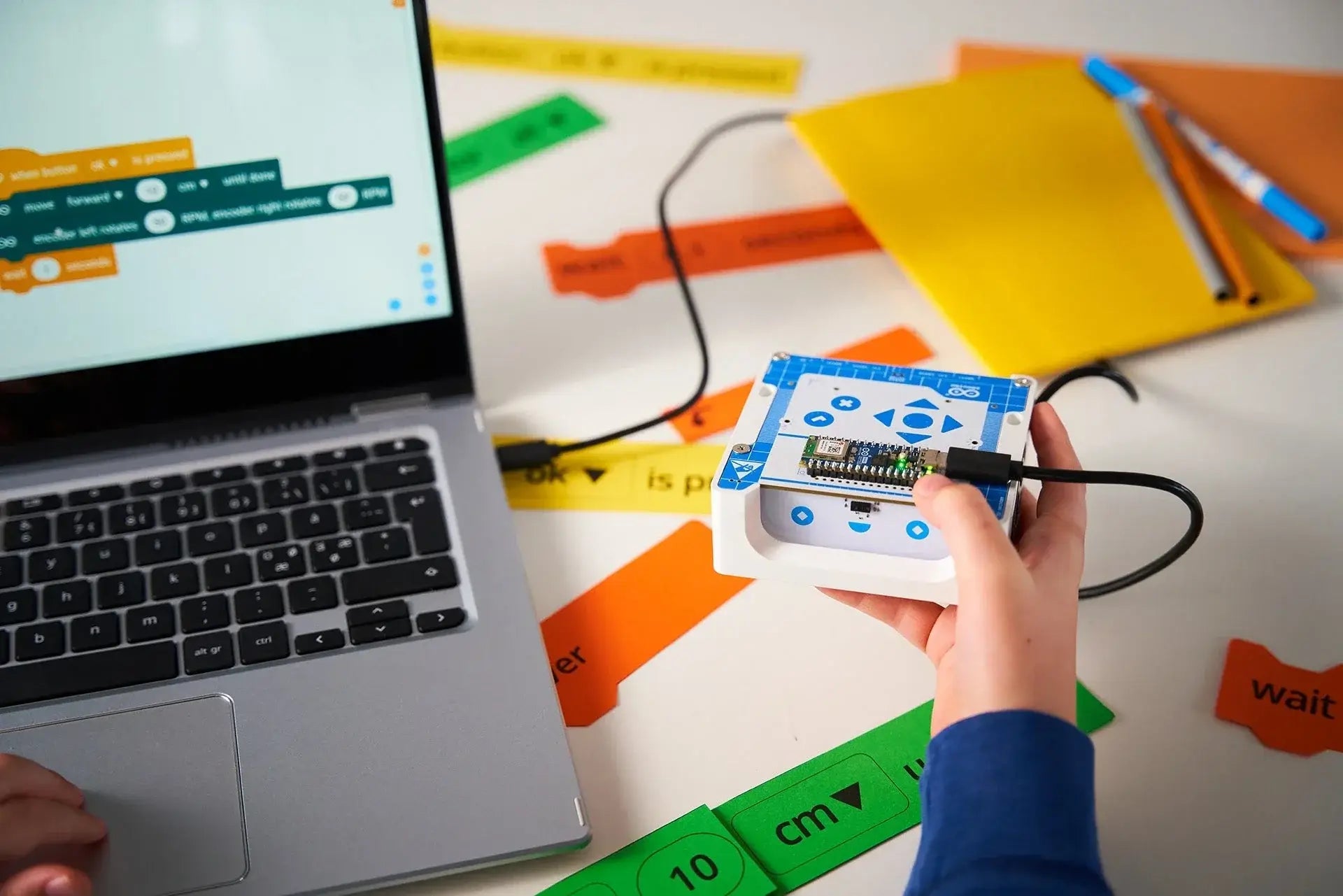 Person using Arduino with a laptop, featuring coding blocks and colorful labels for programming projects.