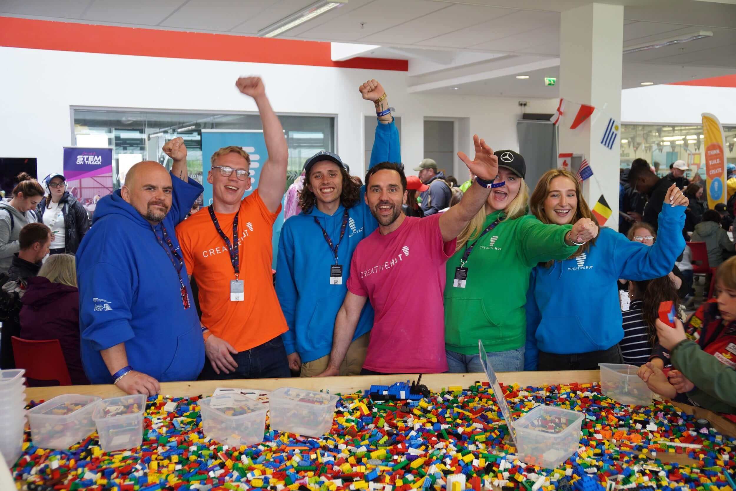 Group of happy people wearing colorful shirts at a Lego activity event, celebrating and engaging with participants.