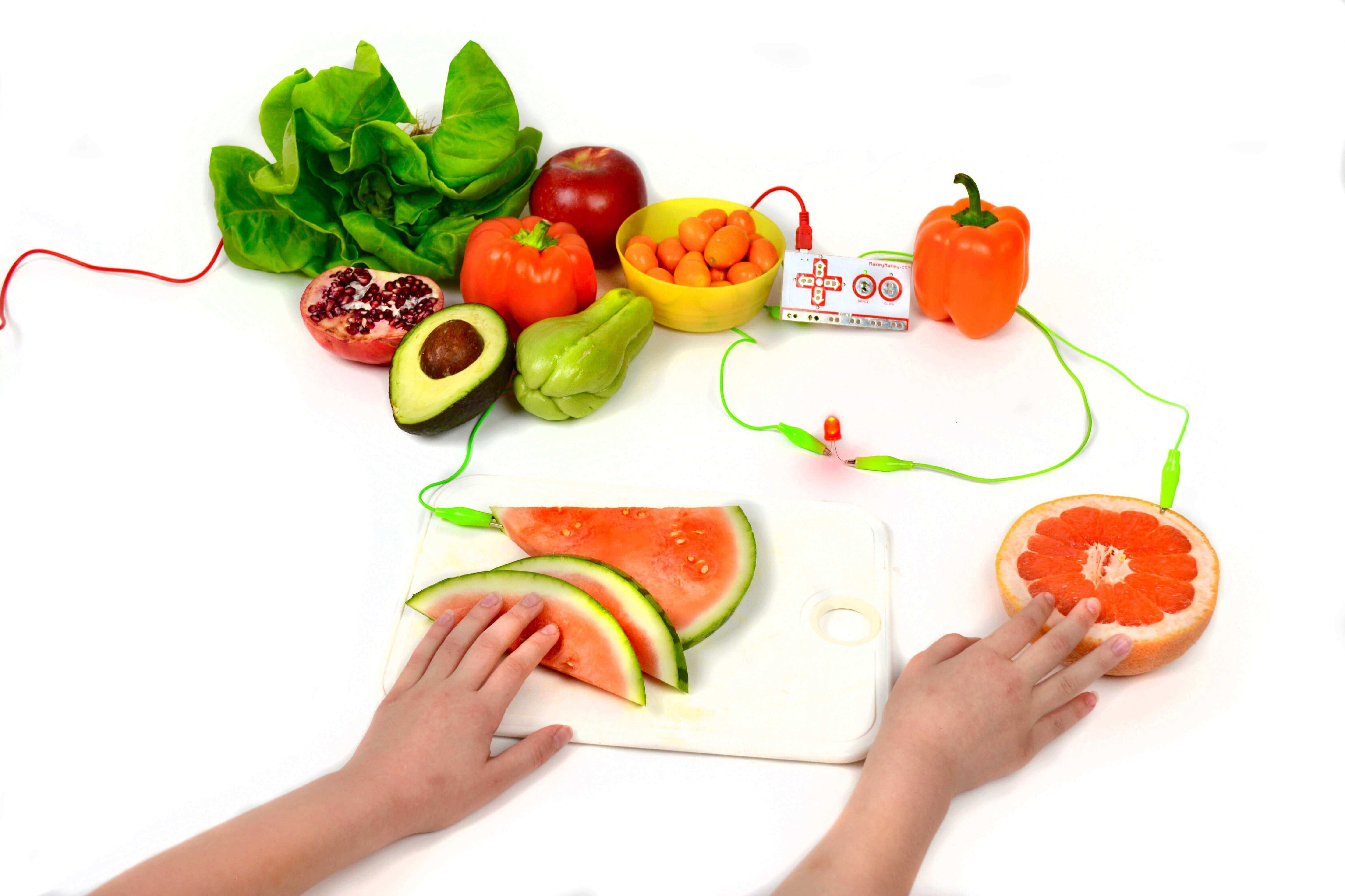 Hands playing with electric fruit and vegetables on a cutting board, showcasing interactive play and learning.