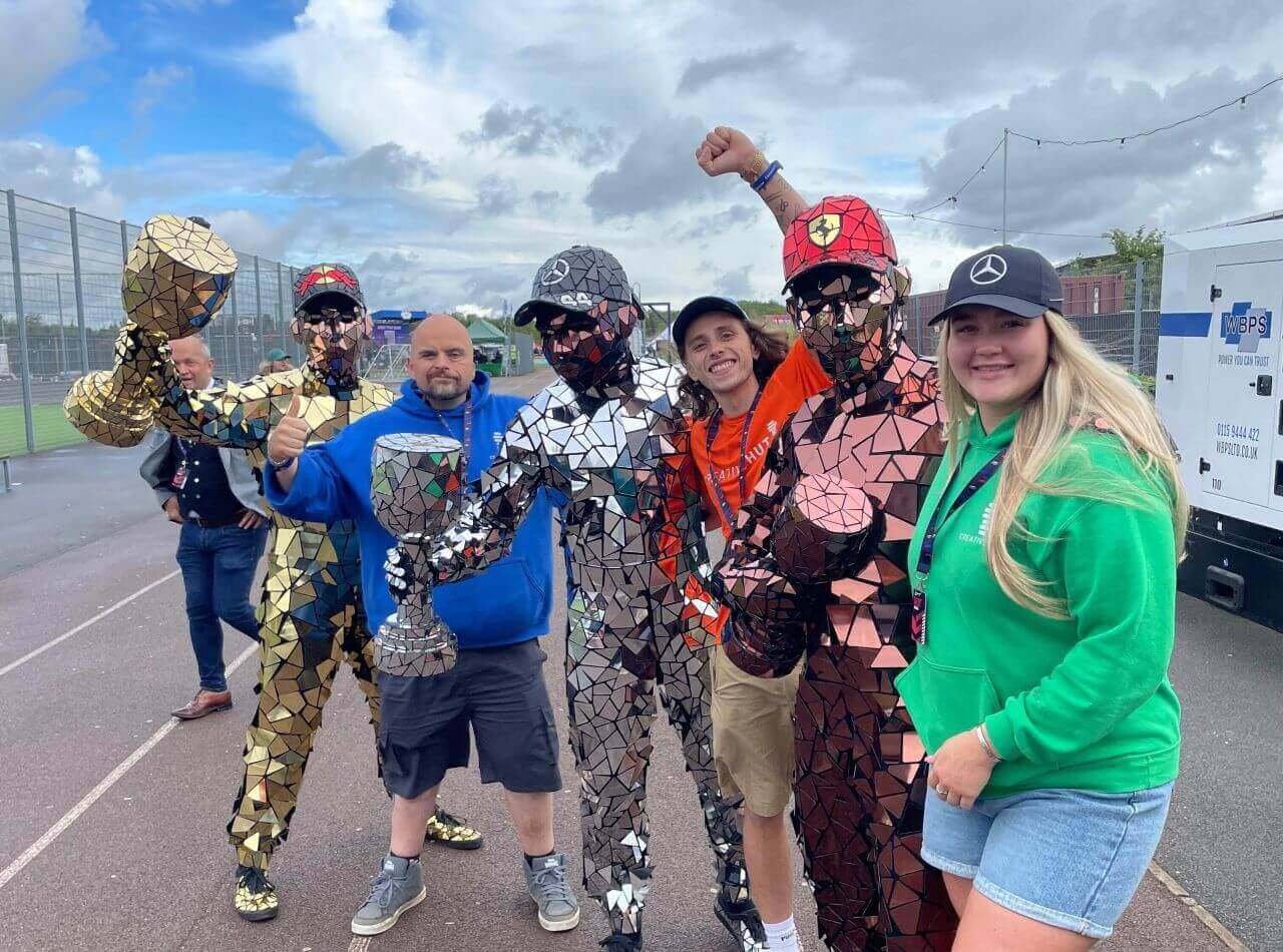 Group of people posing in mirrored outfits, celebrating with trophies at an outdoor event.