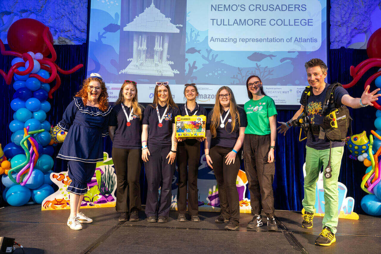 Group of six winners from Tullamore College celebrate Atlantis-themed achievement at event with colorful decorations.