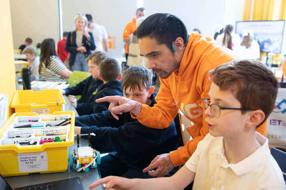 A mentor guides children in a robotics workshop, showcasing creativity and teamwork through coding and building projects.
