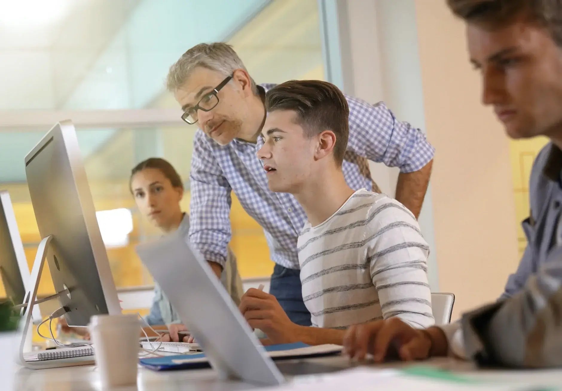 A teacher assists students during a computer class, fostering collaboration and learning in a modern classroom setting.