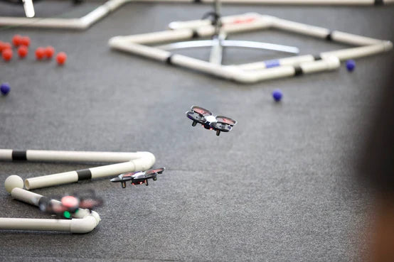 Drones flying over a competition course with obstacles made of pipes and colorful balls on the ground.