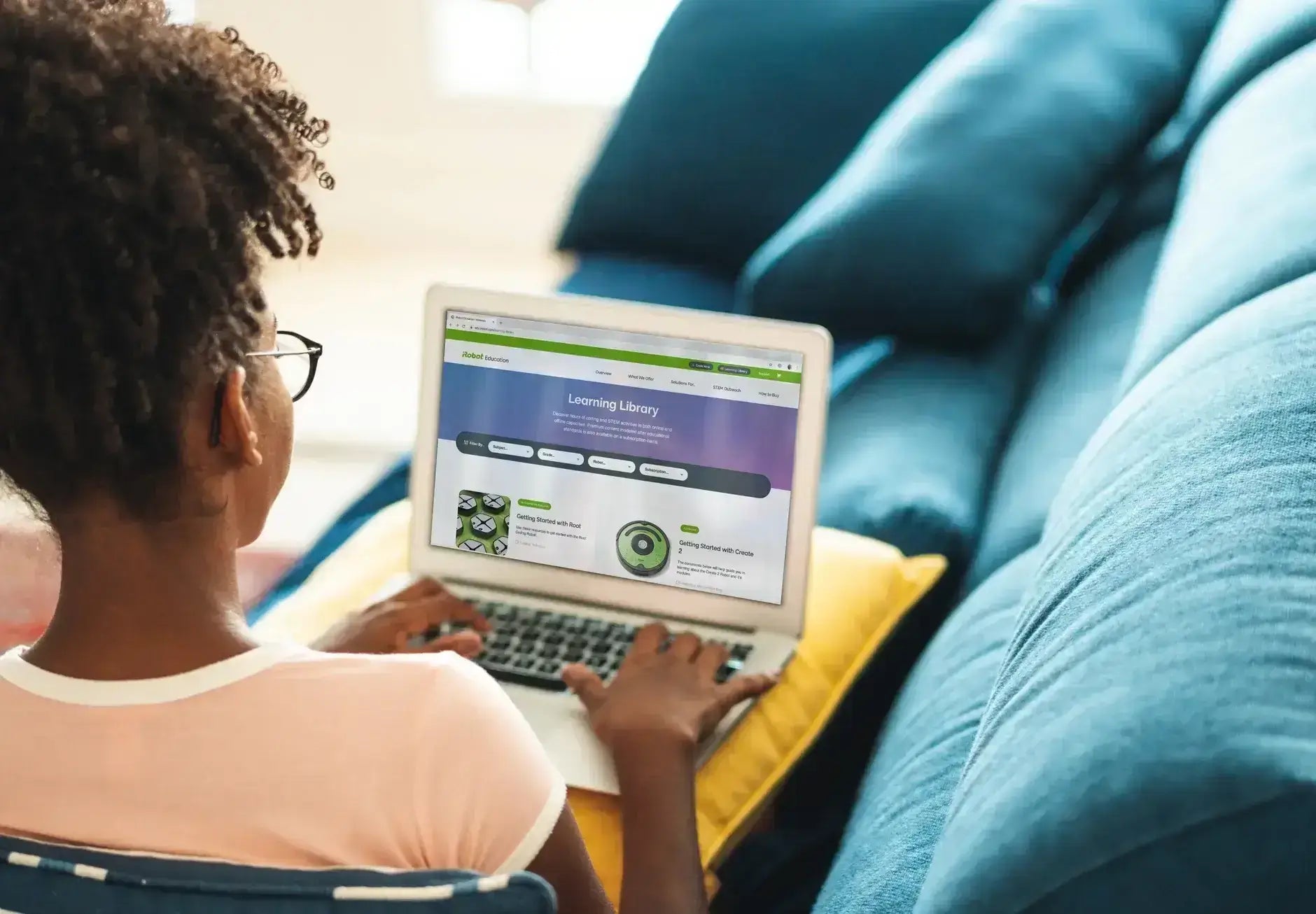 A girl using a laptop on a couch, exploring the Learning Library website for educational resources.