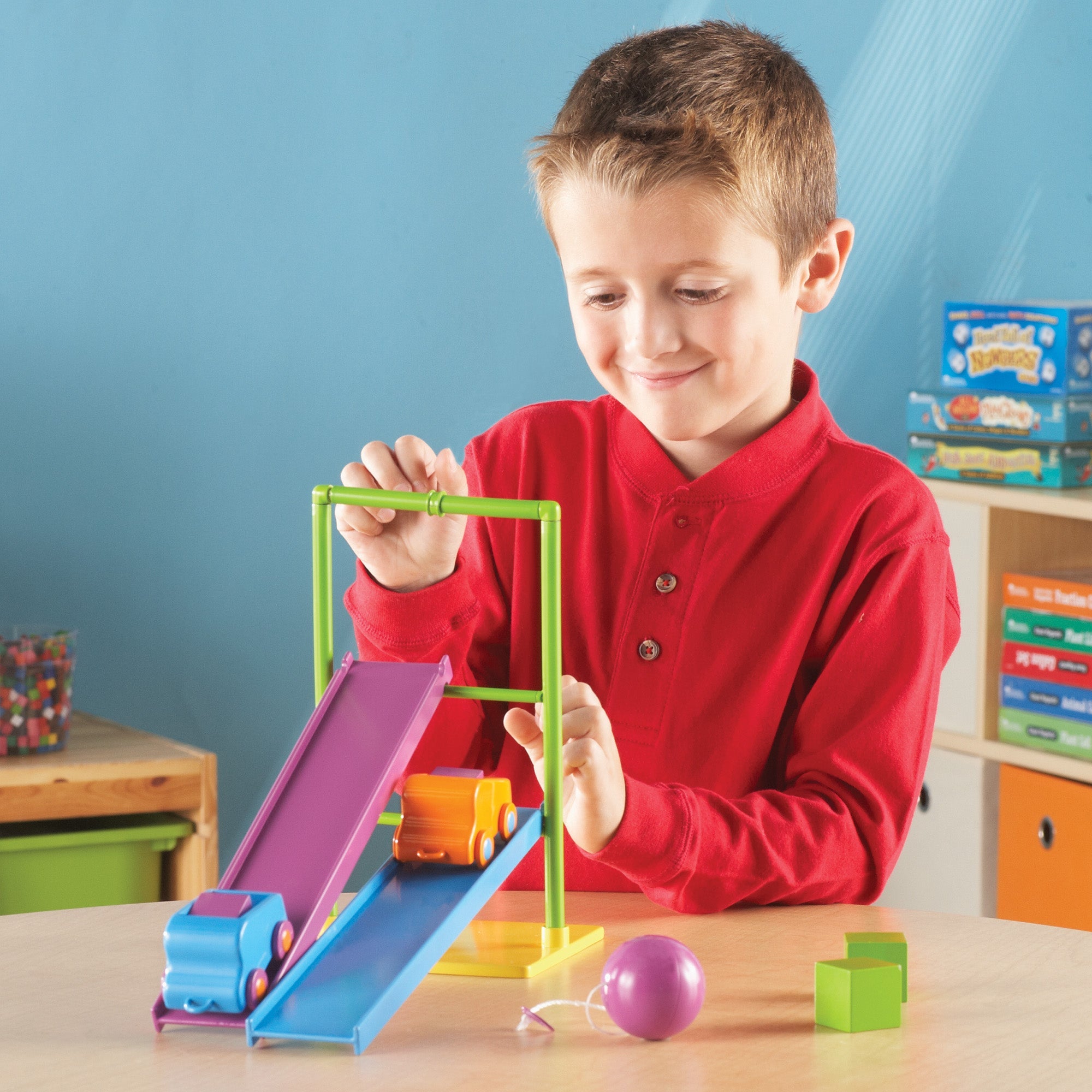 A child in a red shirt experimenting with ramps and toy cars from the Simple Machines set. The scene highlights early engineering and problem-solving investigations.