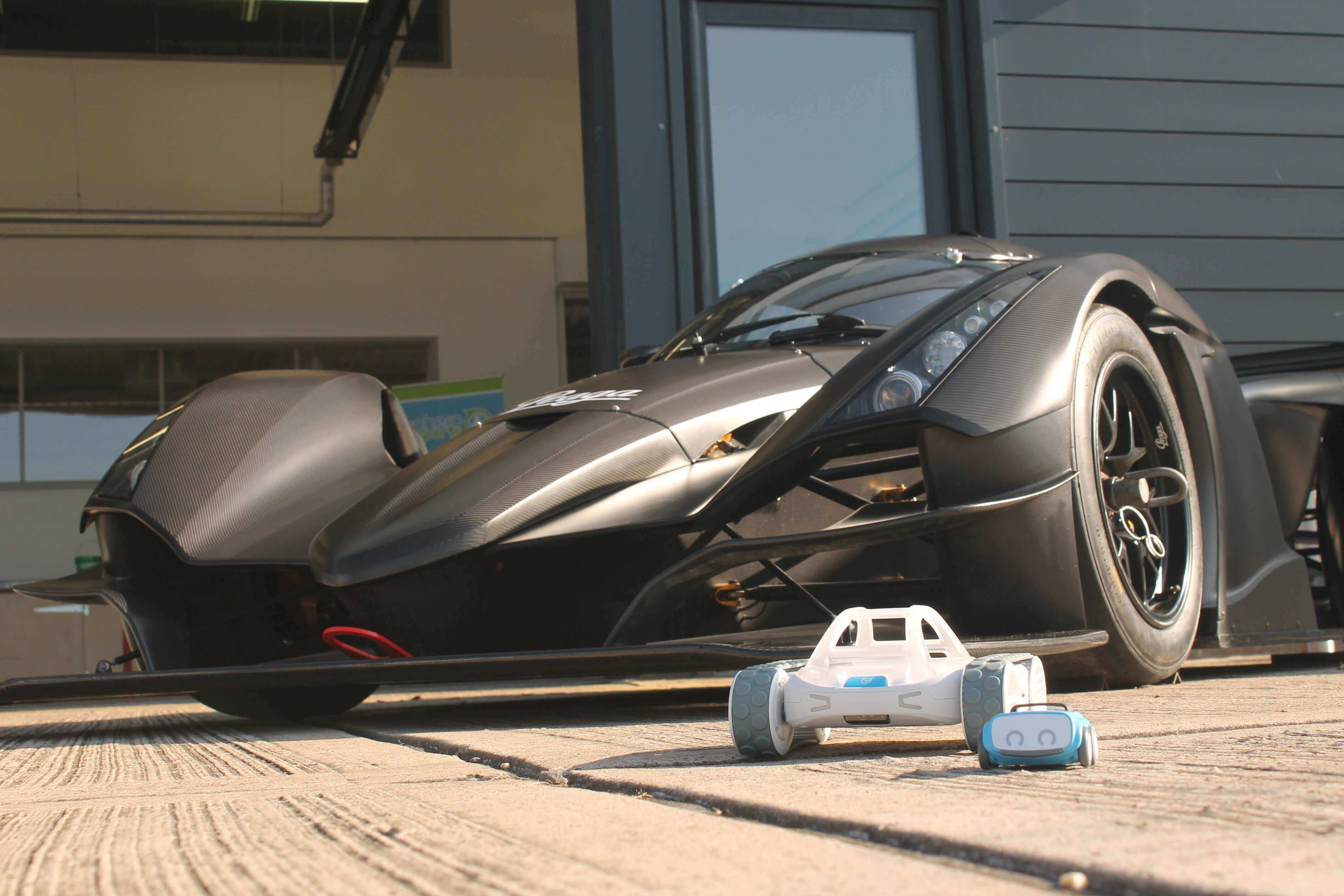 Close-up of a sleek black supercar and a small toy car on a garage floor.