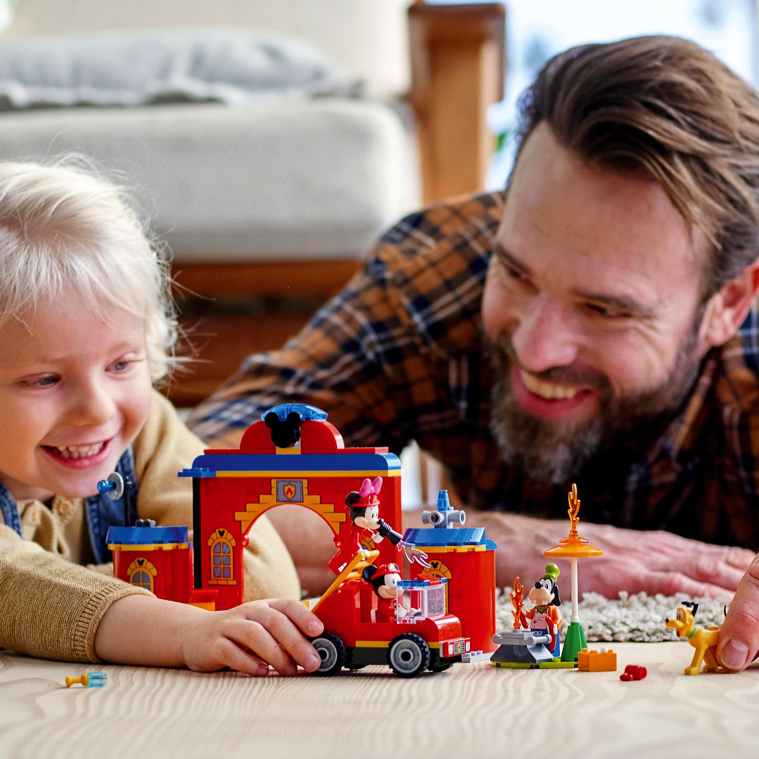 Father and son happily playing with LEGO® Disney Mickey Mouse Fire Engine set, featuring minifigures and fire station.
