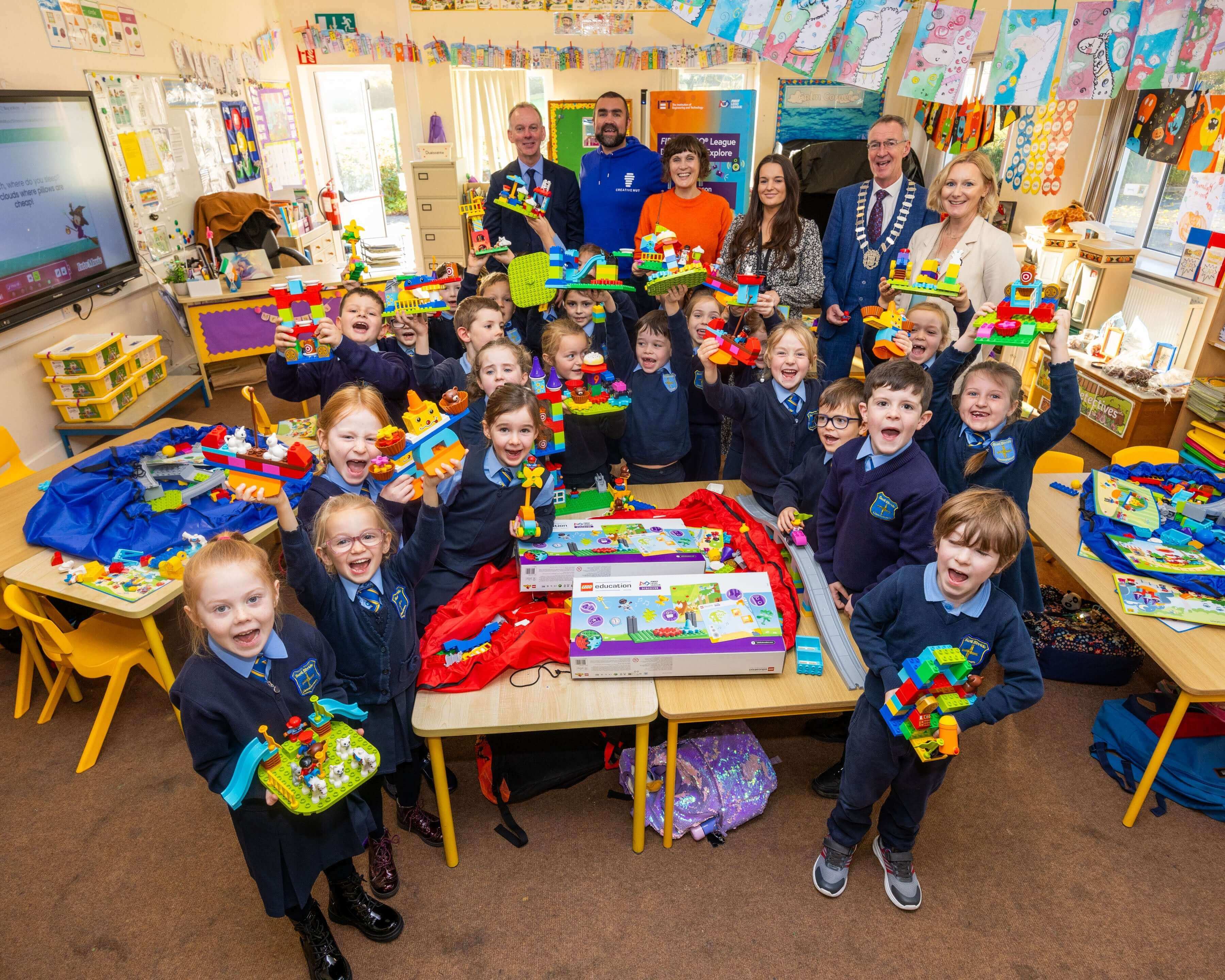 Group of children in a classroom holding colorful building toys, smiling and celebrating creativity.