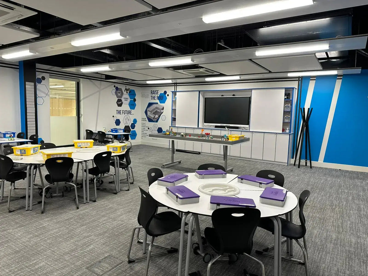 Modern classroom with round tables, purple notebooks, and interactive display wall, promoting collaborative learning.