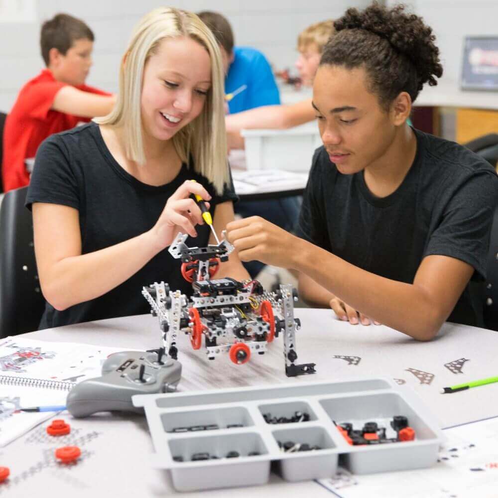 Two students collaboratively building a robot with TETRIX components, showcasing teamwork and engineering skills.