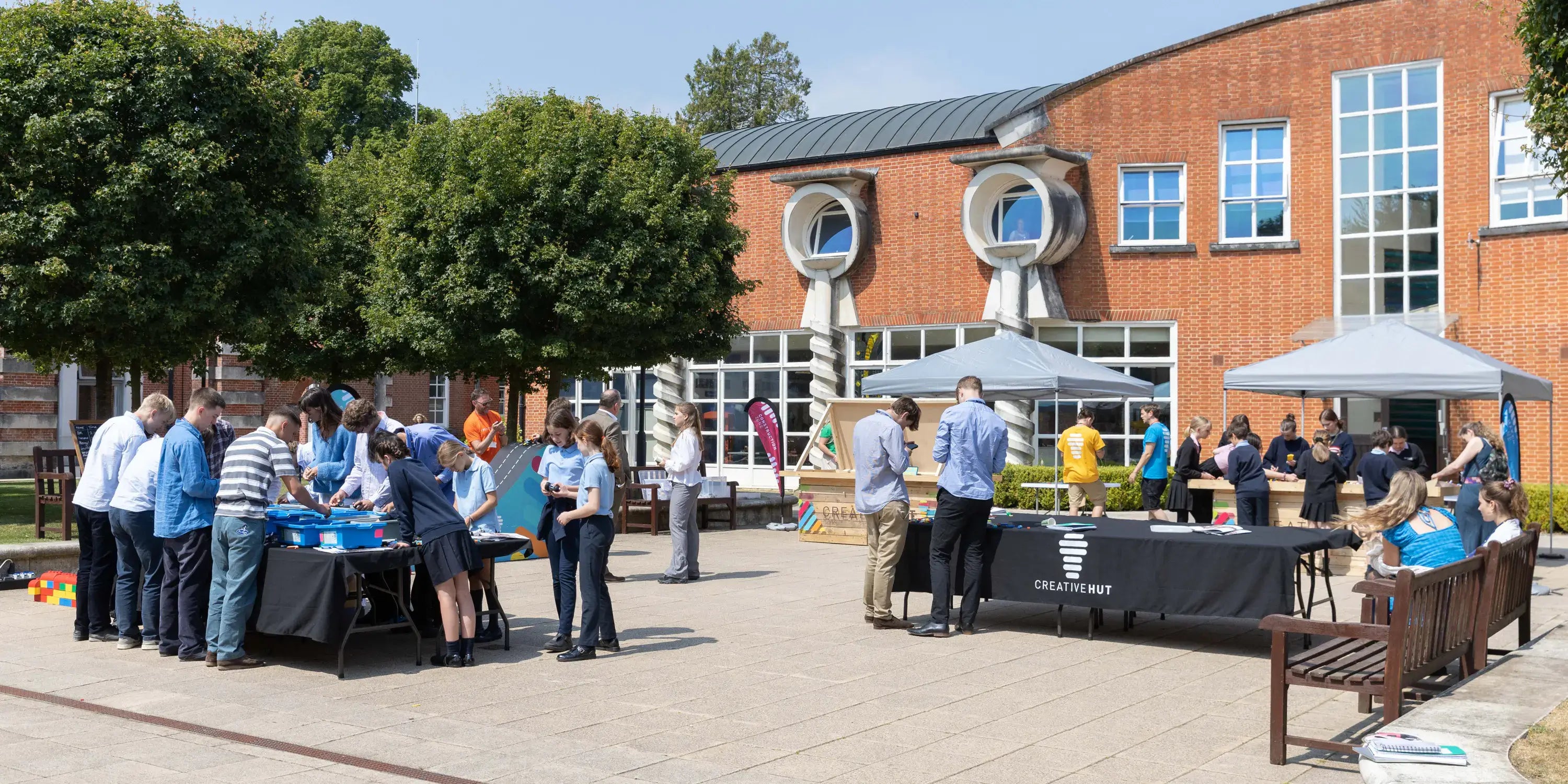 Community gathering in a sunny courtyard with people engaging in activities at tables and tents.