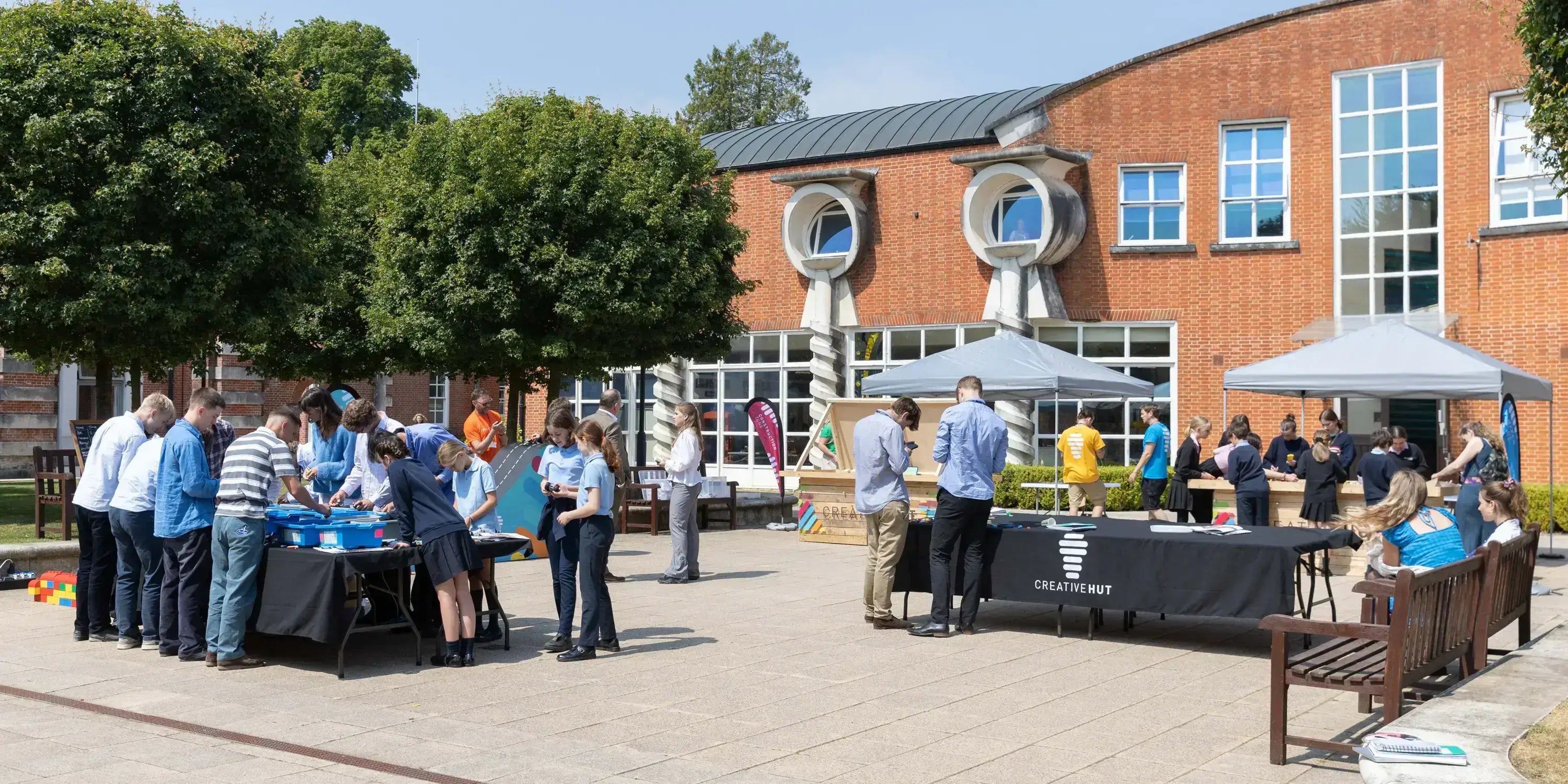 Community gathering in a sunny courtyard with people engaging in activities at tables and tents.