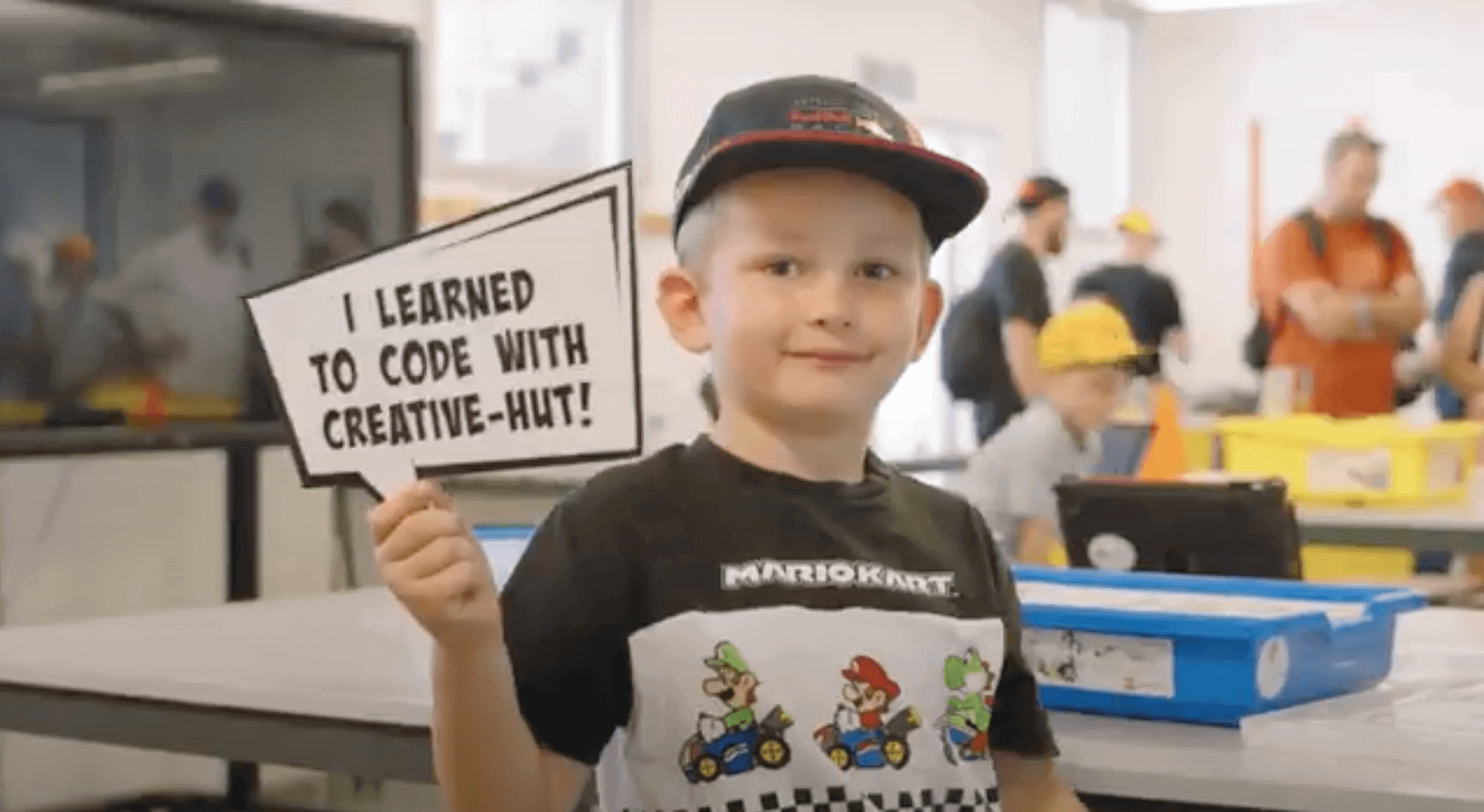 Young boy holding a sign saying 'I learned to code with Creative-Hut' at a coding workshop.
