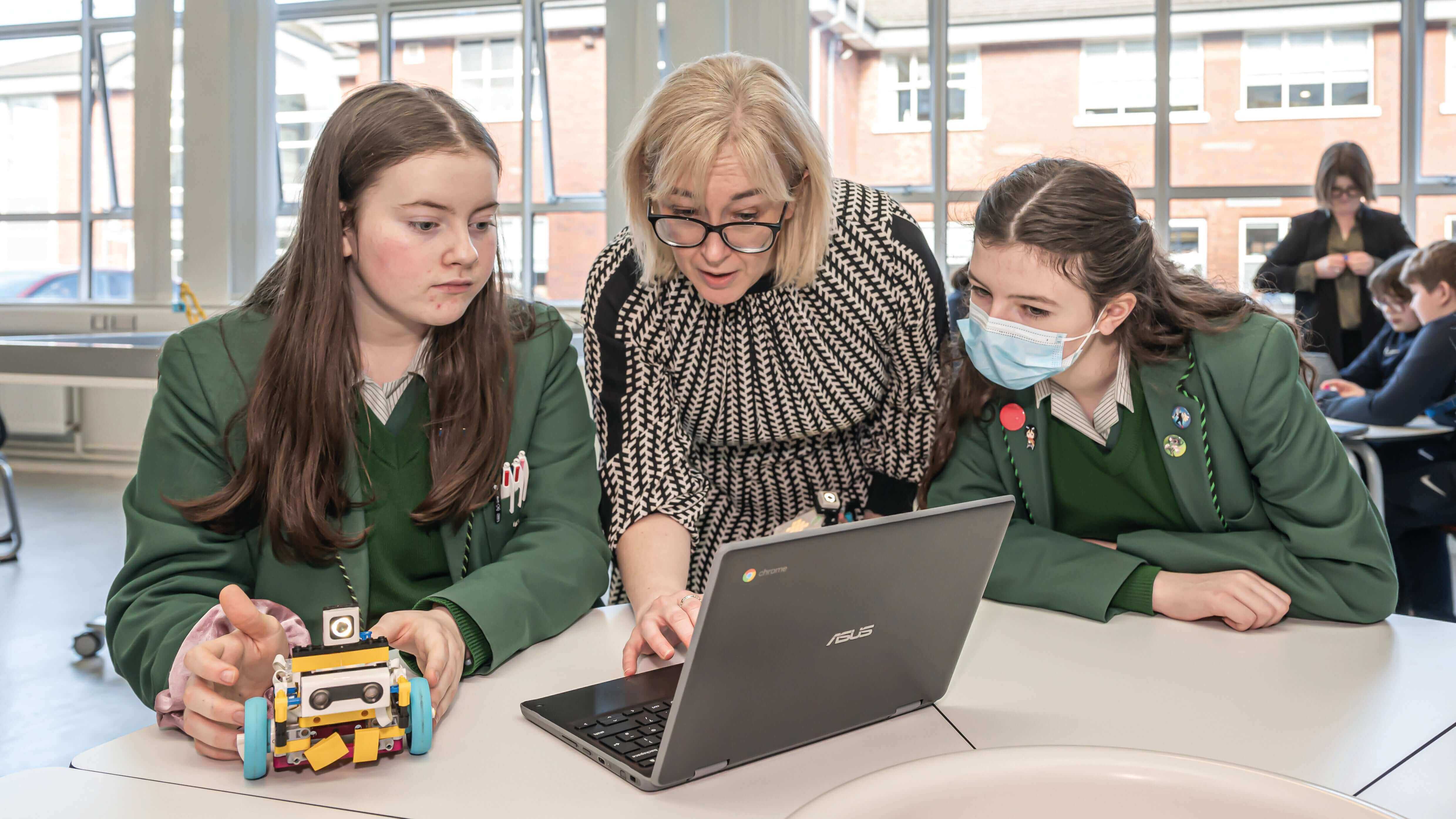 Students collaborating with a teacher on a robotics project using a laptop.