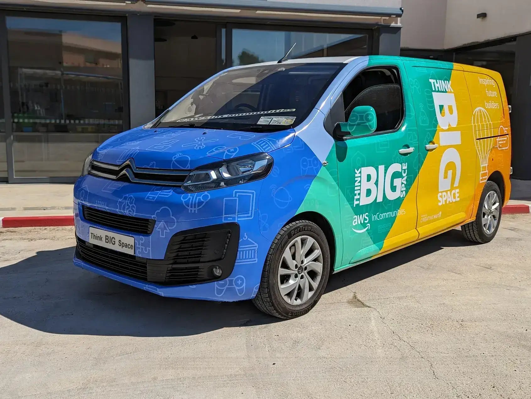 Citroen van wrapped in colorful 'Think BIG Space' graphics, parked outside a building.