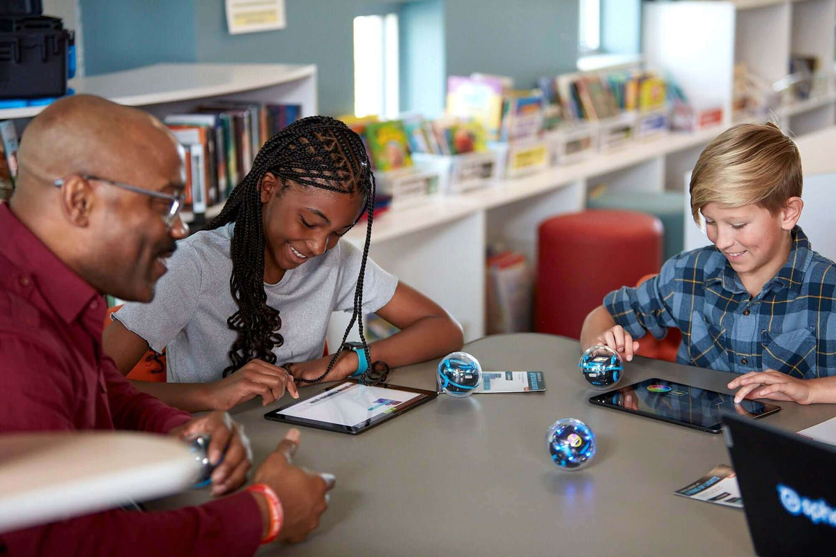 Children and an adult engaging with tablets and robots in a library setting, promoting interactive learning.