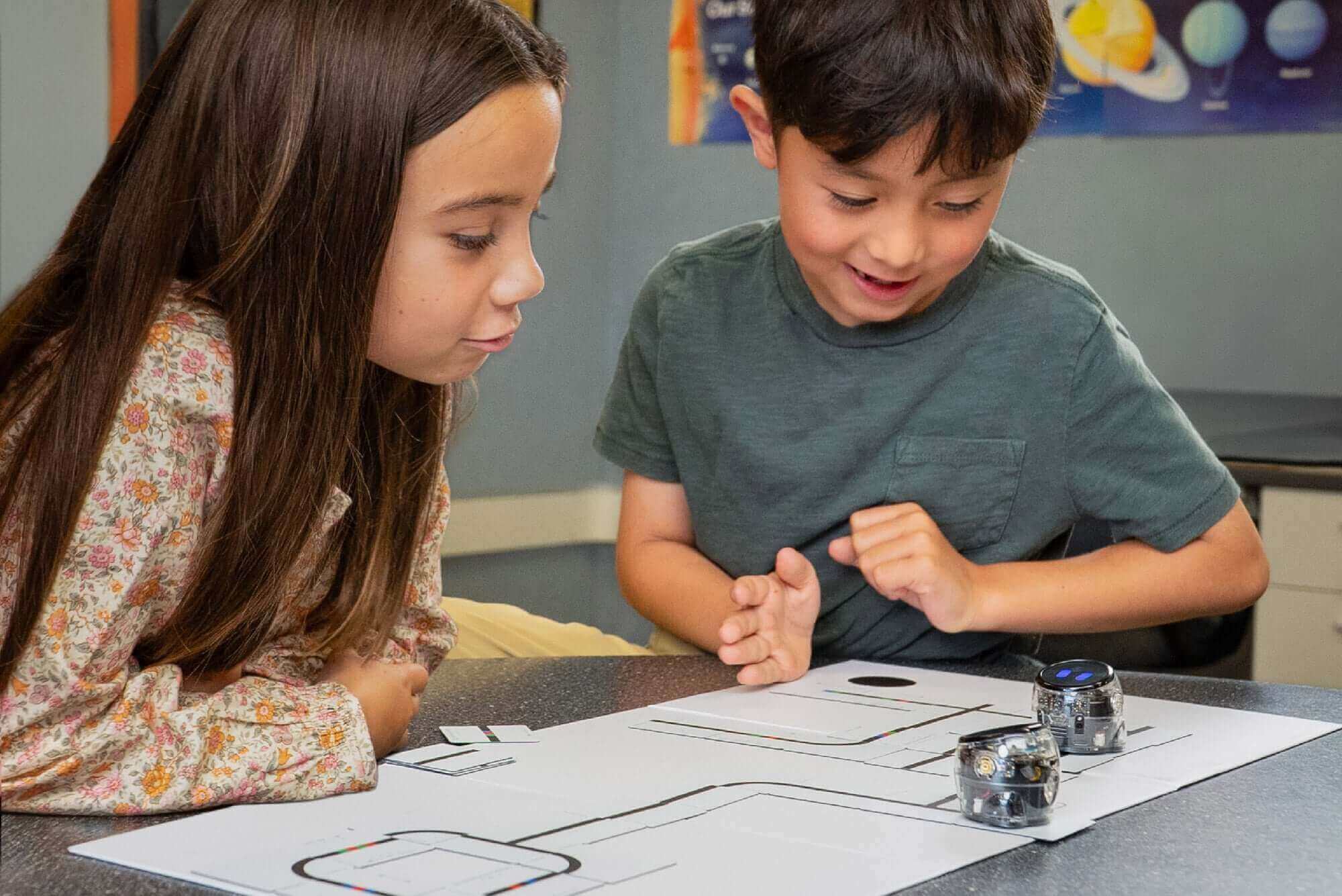 Two children engaged in robotics with a coding activity, observing small robots on a printed path.