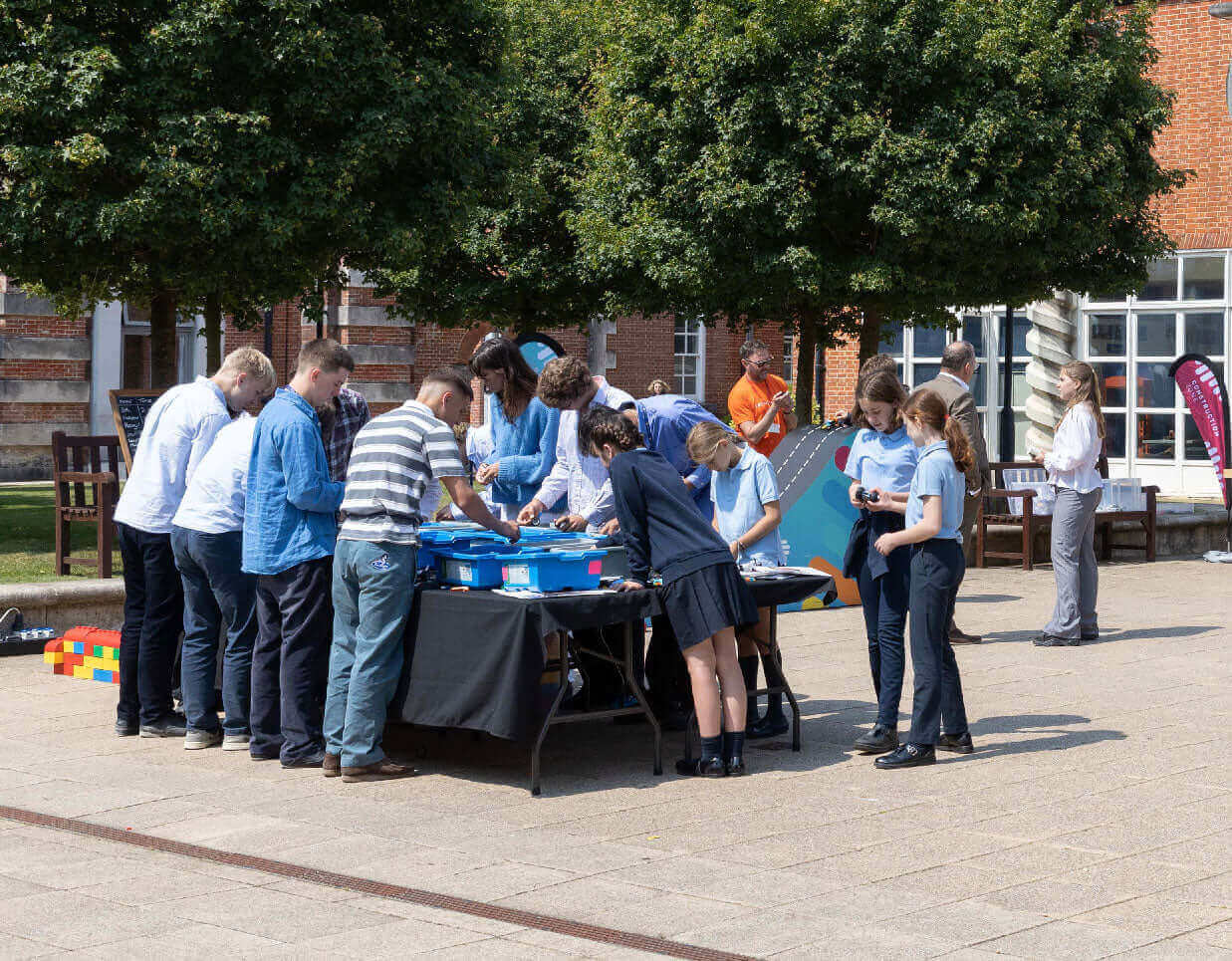 A diverse group of people engaging in activities around a table outdoors on a sunny day.