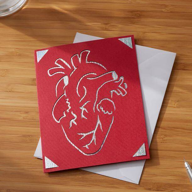 Red greeting card with silver heart design, placed on a wooden surface next to a white envelope.