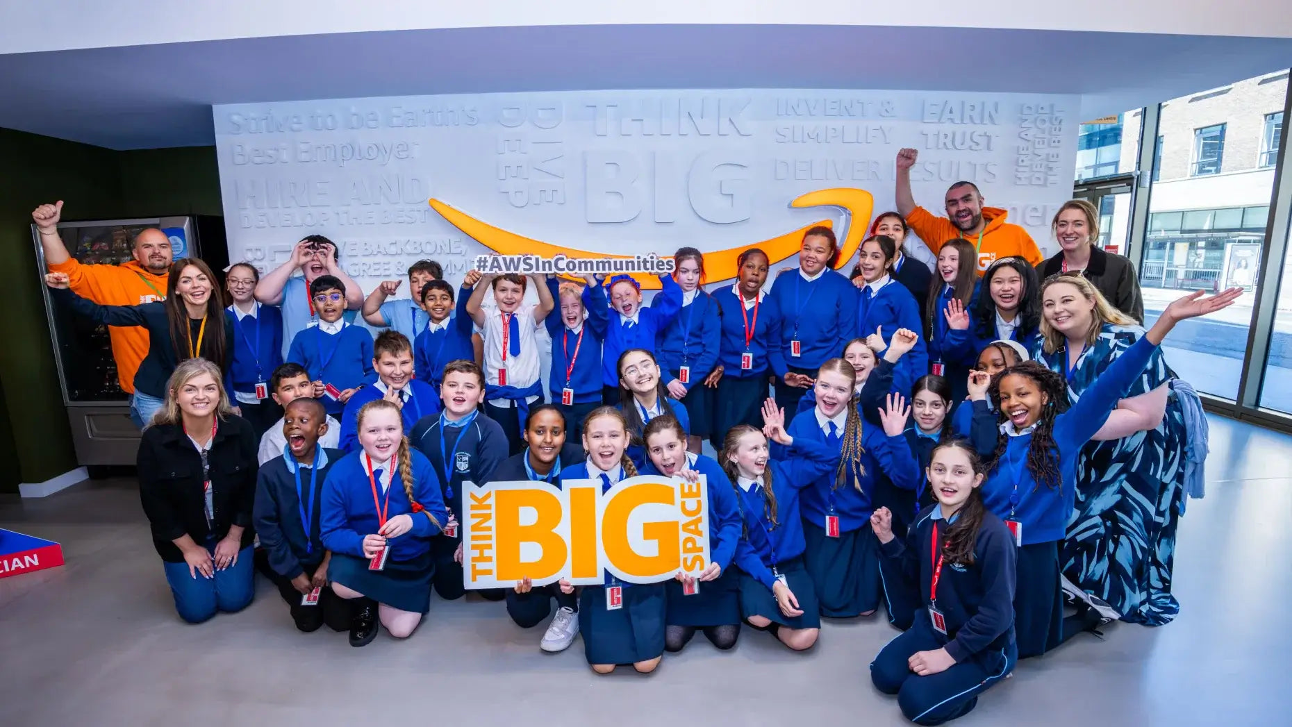 Group of children and adults smiling and posing with 'THINK BIG' sign at community event.