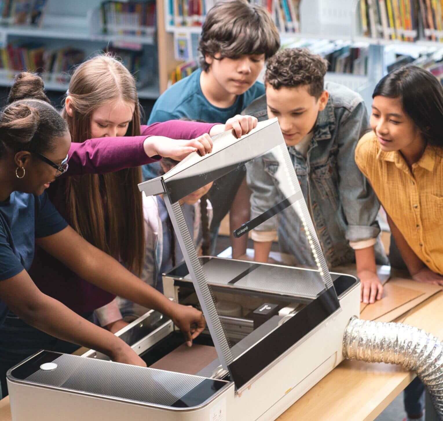 Students engaged in hands-on learning with a laser cutter at a library workshop, fostering creativity and teamwork.