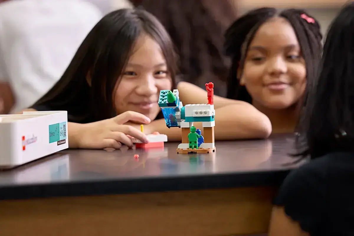 Two girls joyfully engaging with a Lego robotics project in a classroom setting.