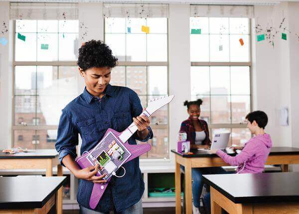 Student using littleBits Code Kit to create a guitar in a classroom setting with peers engaged in projects.