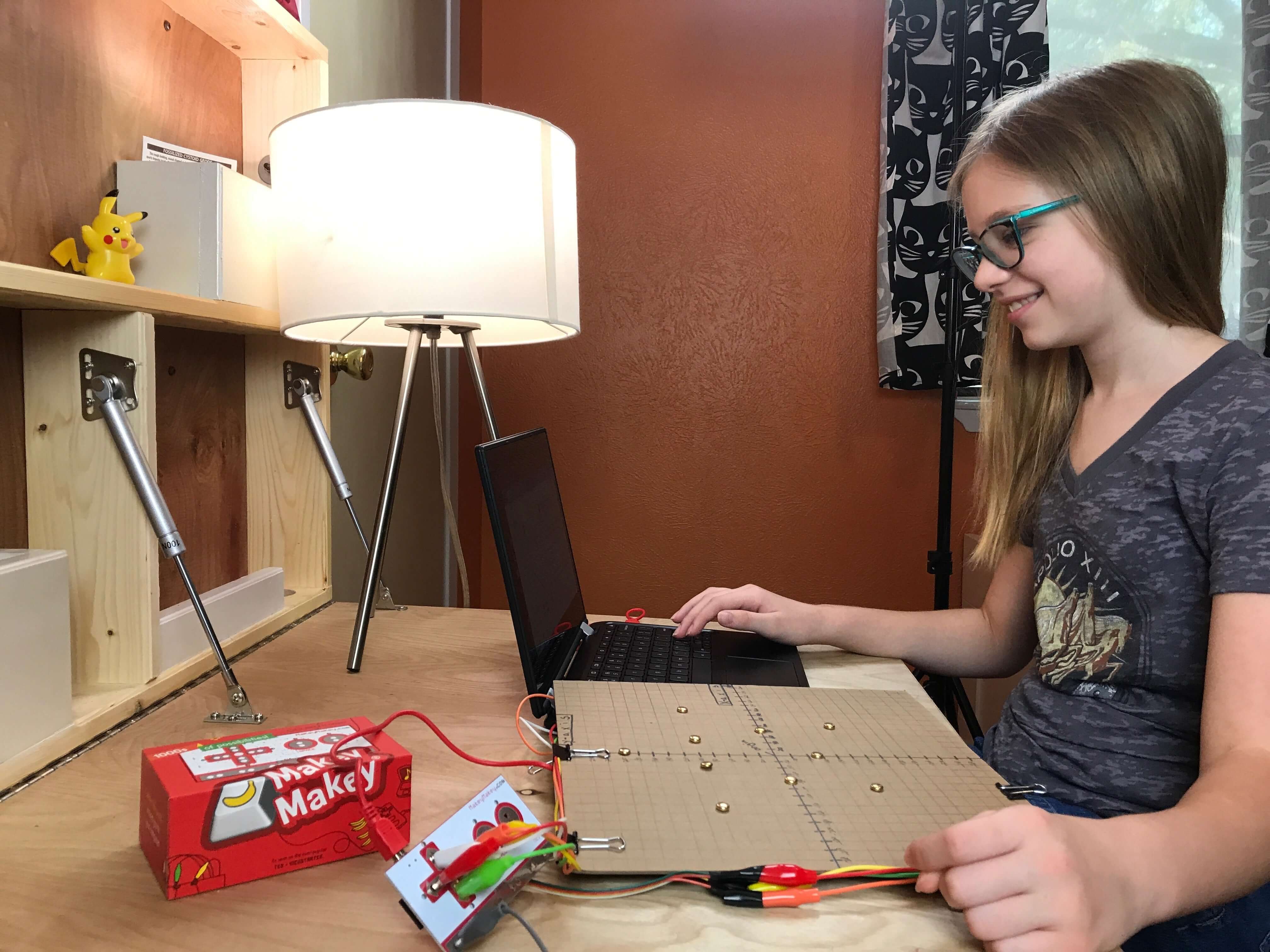 Child using Makey Makey STEM Pack at a desk, with a laptop and a circuit board, inspiring creativity in STEM learning.