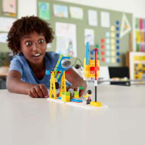 Excited child playing with a colorful LEGO construction set in a bright classroom environment.