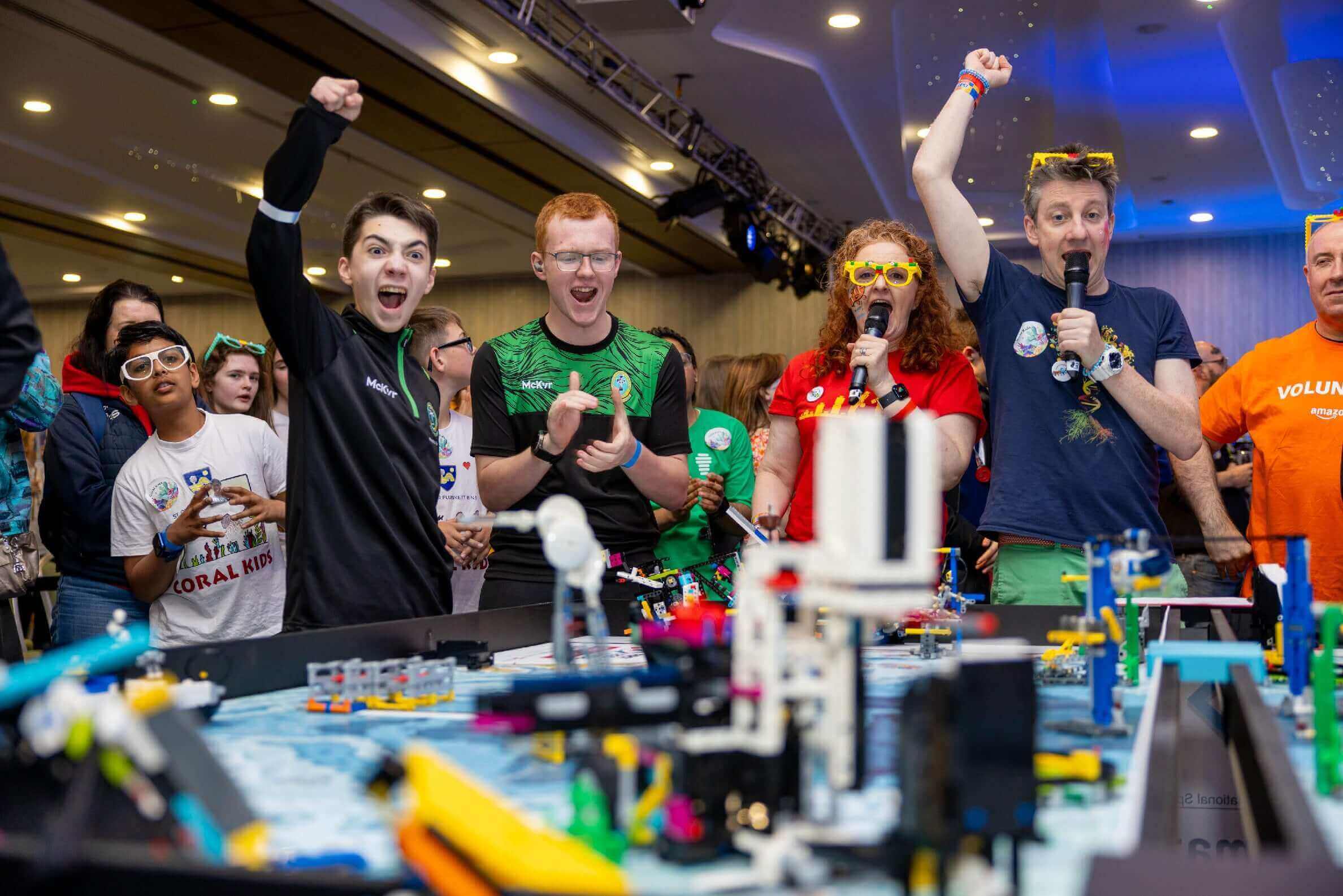Excited participants celebrating at a robotics competition with colorful outfits and props.