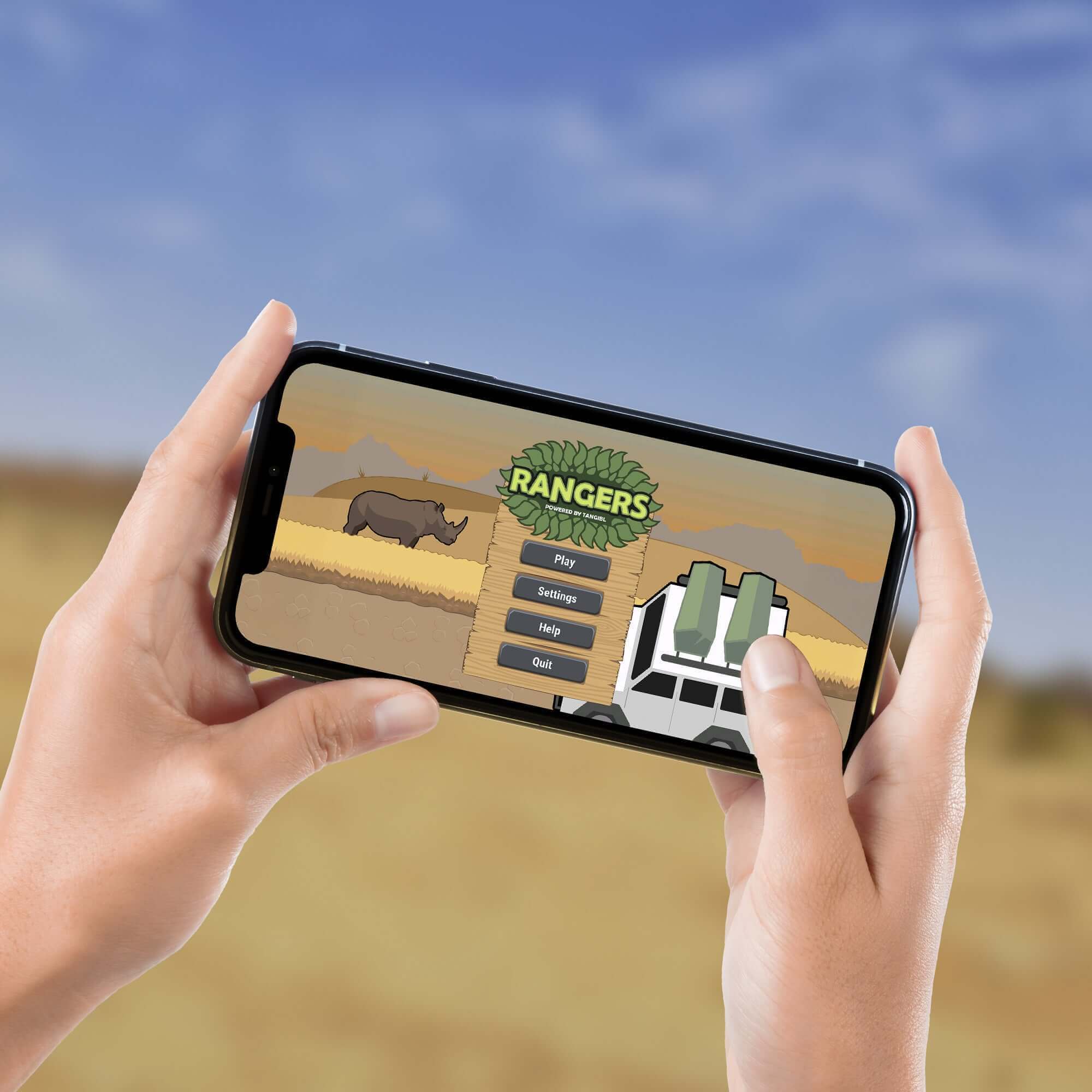 Person holding a smartphone displaying a wildlife game featuring a rhino and game options like 'Play' and 'Help' in a natural setting.