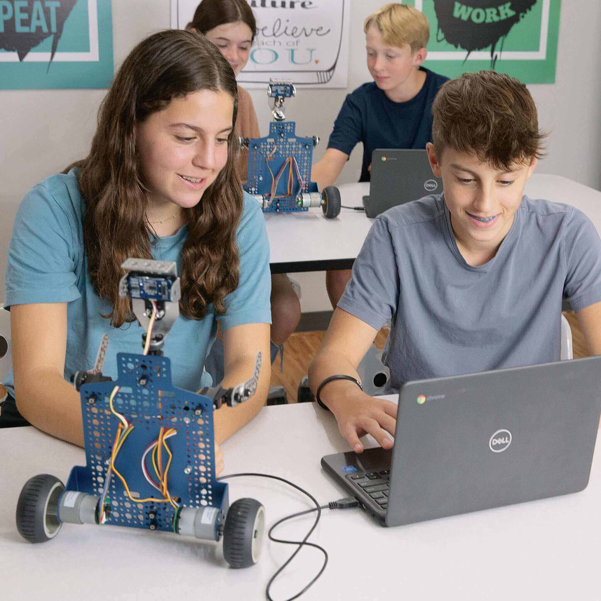 Two middle school students engaging with a Seeker robot and a laptop, exploring coding and robotics in a classroom.