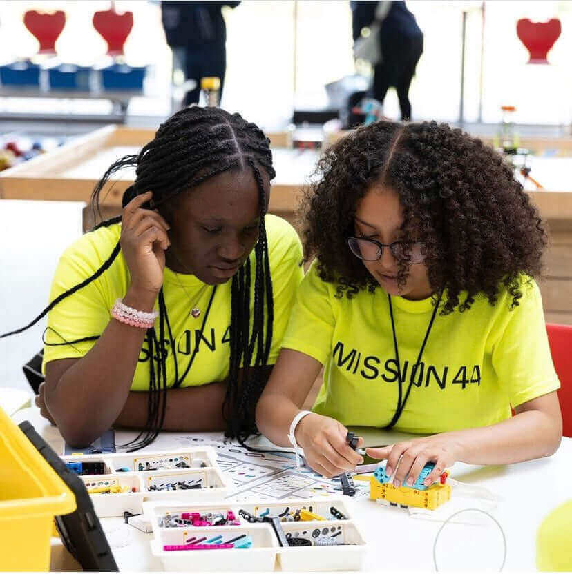 Two young girls in bright yellow shirts focused on a STEM project with colorful building materials.