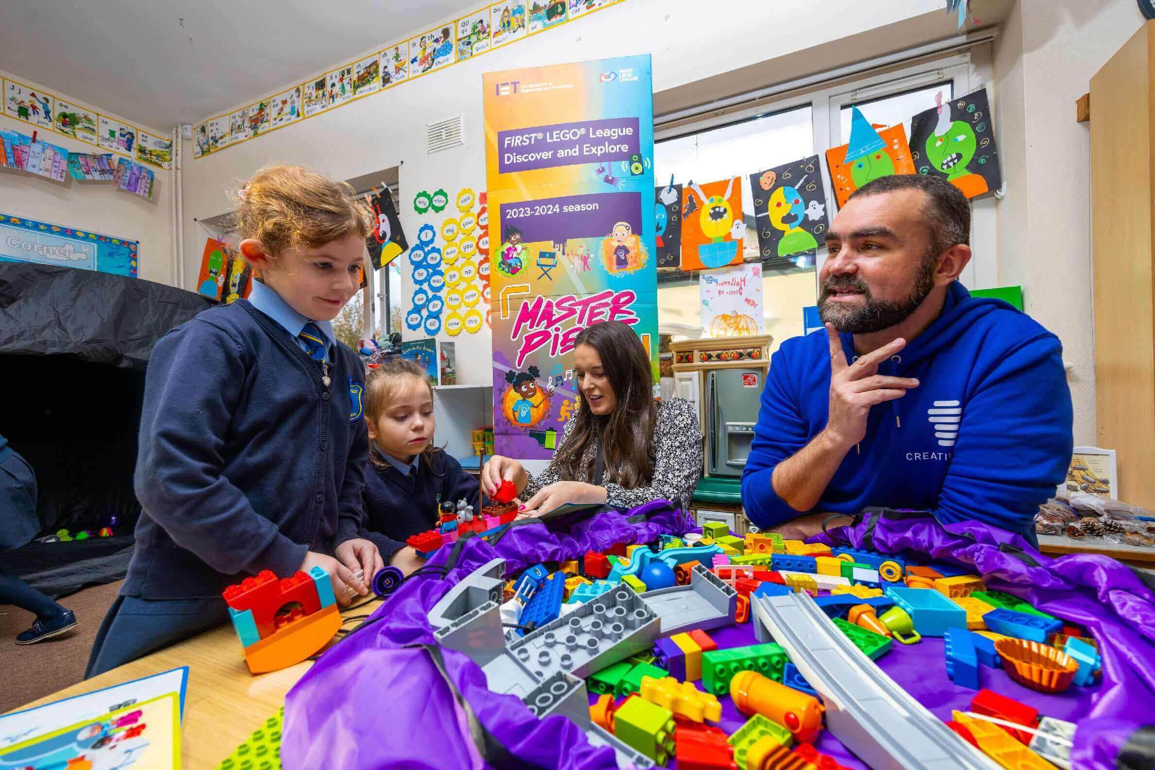 Children and an adult engaged in LEGO building activities at a workshop with colorful educational banners.