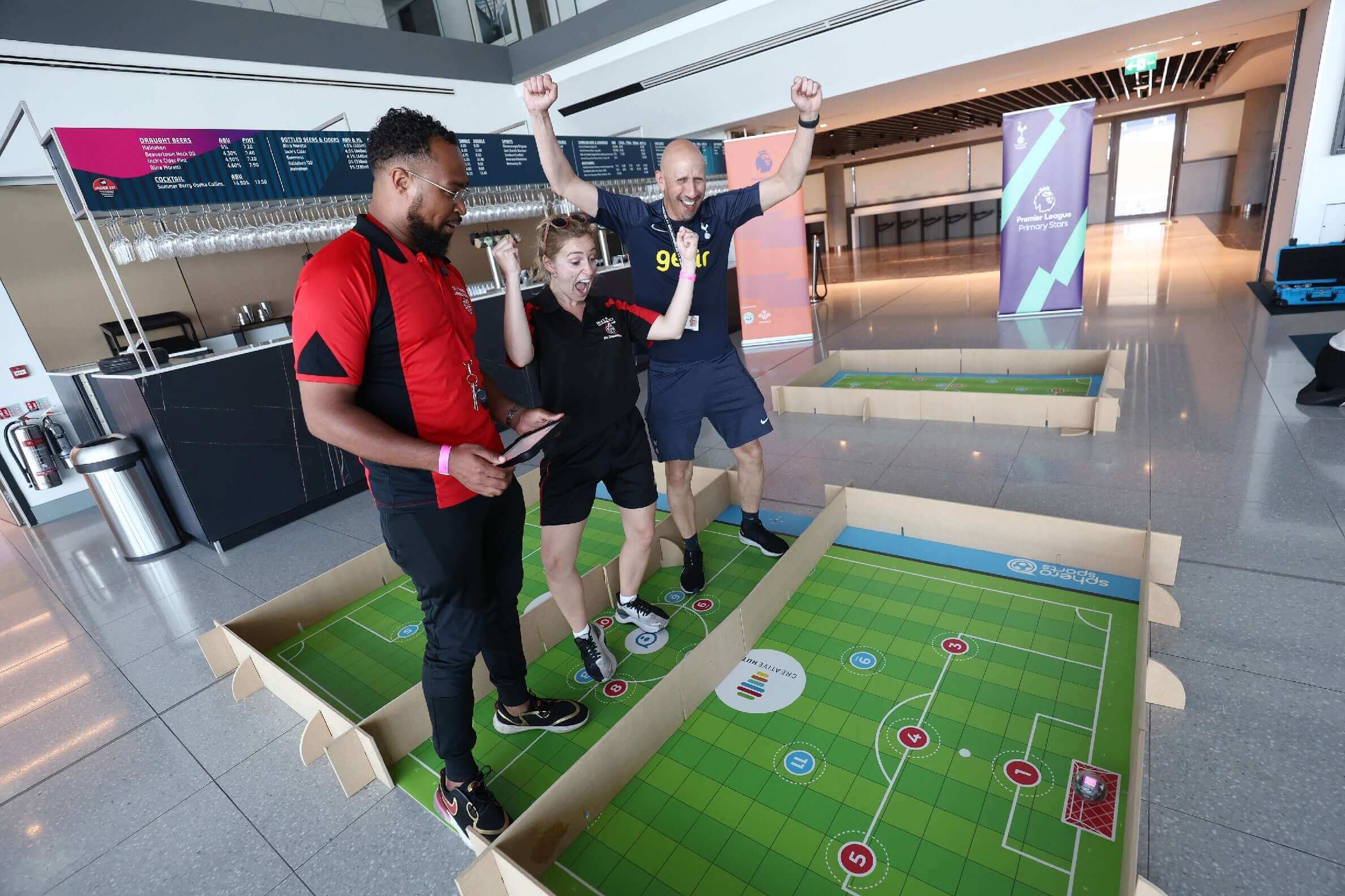 Three engaged participants excitedly playing a tabletop soccer game in a modern venue.