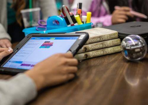 Student using a tablet for block programming in a computer science foundation course with educational materials.