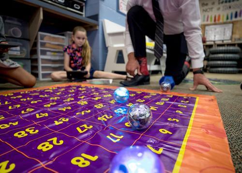 Students using Sphero robots on a colorful coding mat in a classroom setting.