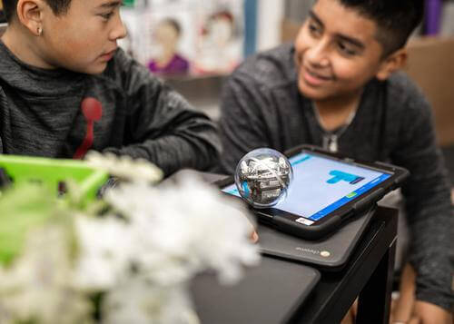 Two students collaborate with a Sphero robot and tablet, engaging in block programming activities.
