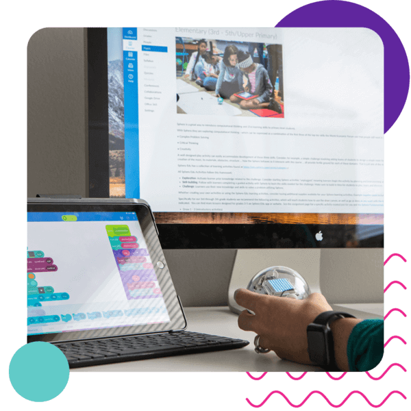 Person interacting with a Sphero robot while using a tablet for block programming in a learning environment.