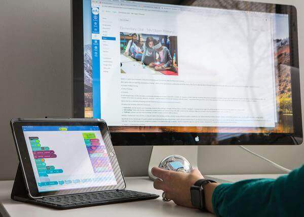 Person using tablet with coding interface alongside a computer showing educational content about Sphero.