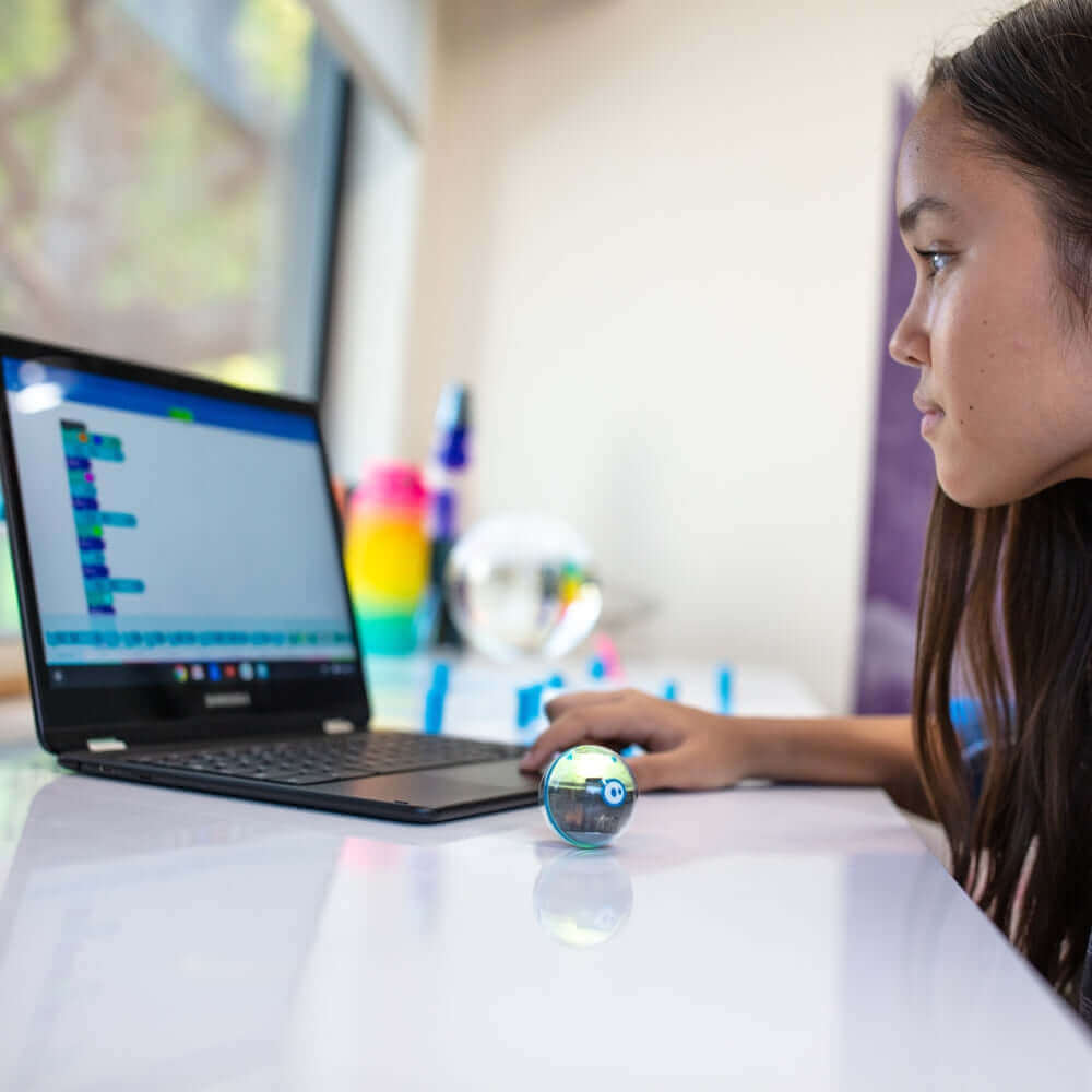 A girl coding with Sphero Mini Robot beside her laptop, showcasing interactive tech and fun learning.