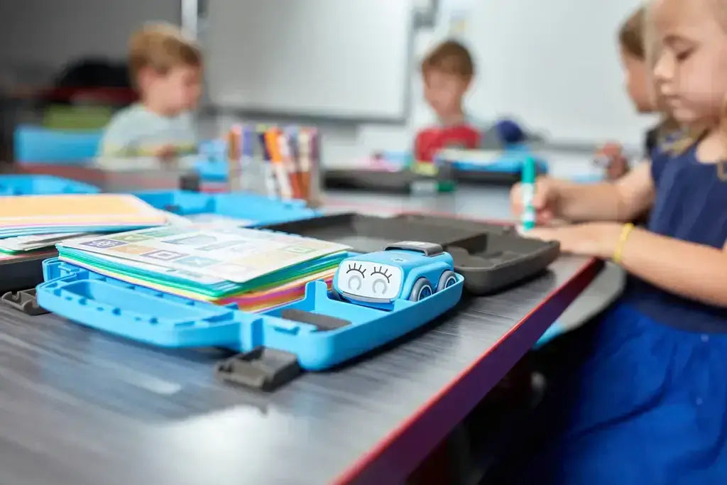 Children engaged in hands-on learning activities, with colorful materials and a blue educational tool on a classroom table.