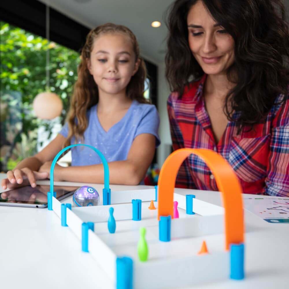 Mom and daughter playing with Sphero Mini, obstacle course with colorful game components, engaging in STEM learning.