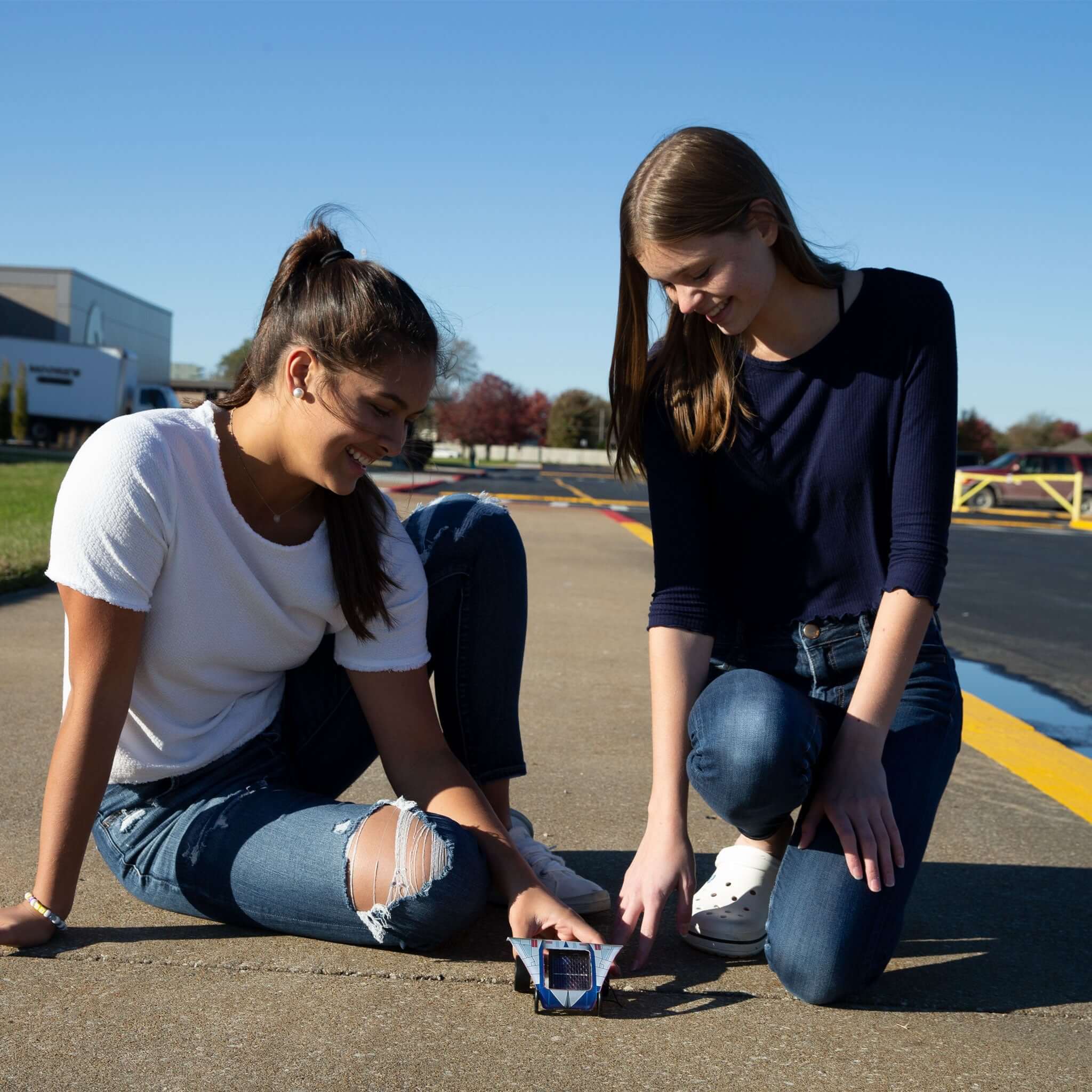 Two young women assembling and testing the Sunezoon solar car kit outdoors on a sunny day.