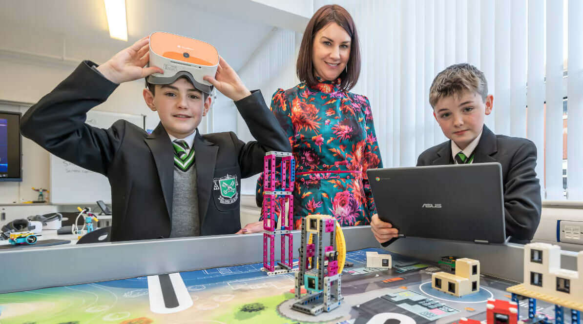 Students engaging with technology in a classroom, using VR headsets and laptops for learning.