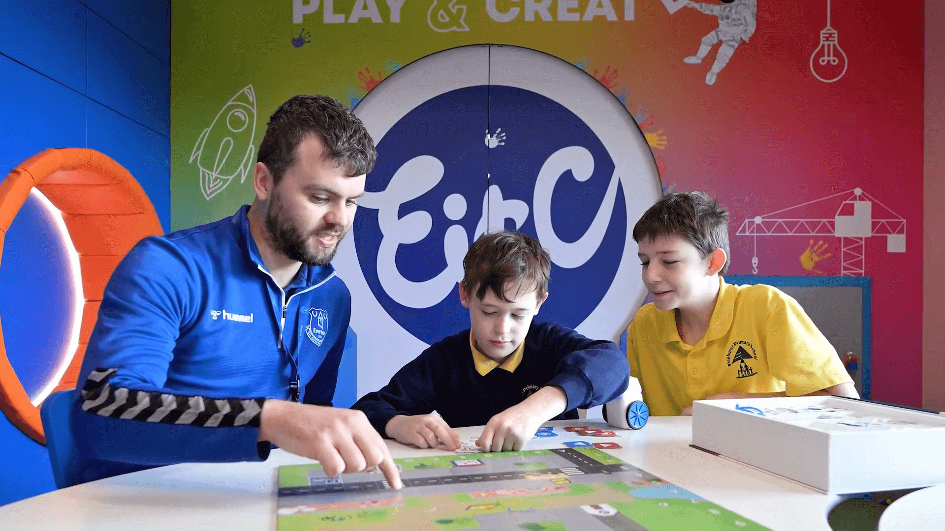 A man and two boys engage with a board game at a colorful educational center, promoting creativity through play.