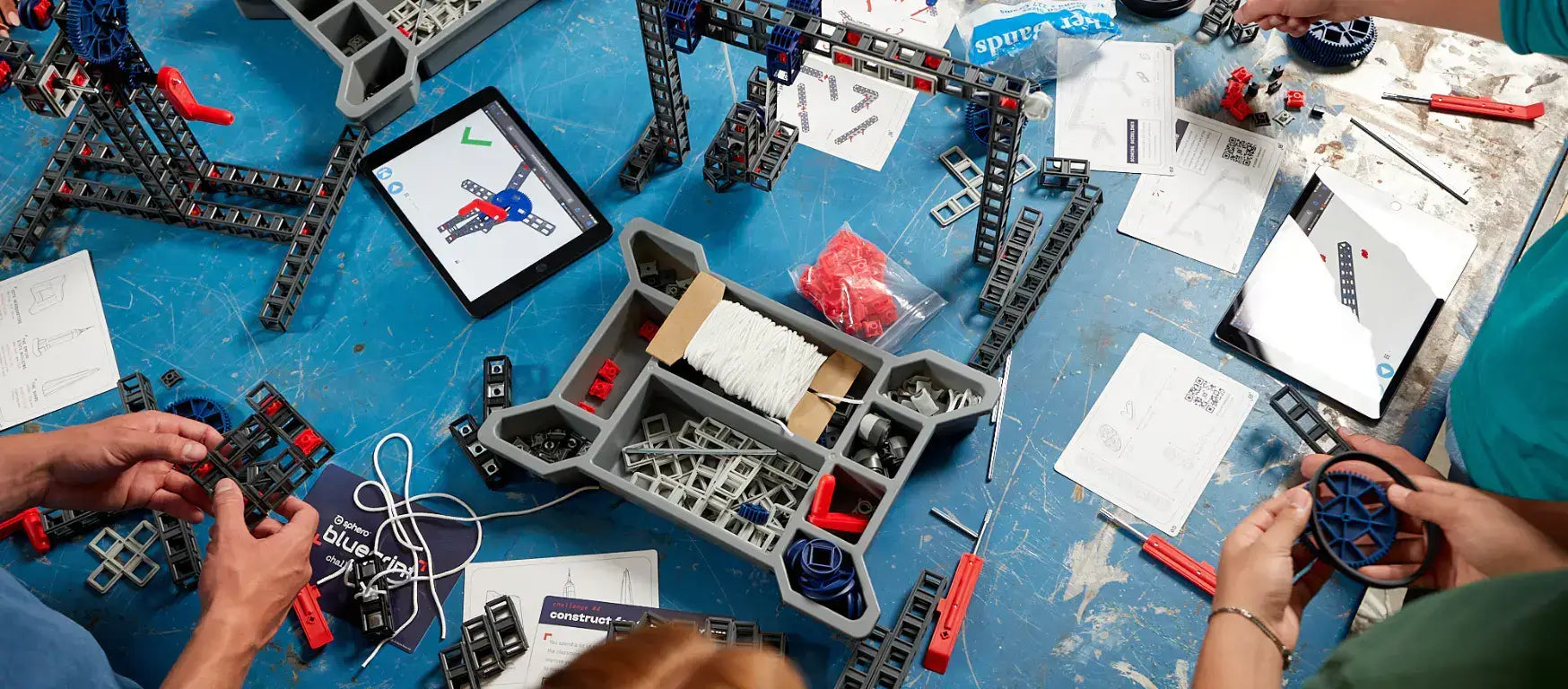 Students building with modular Sphero Blueprint parts on a work table, with an iPad and instruction materials.