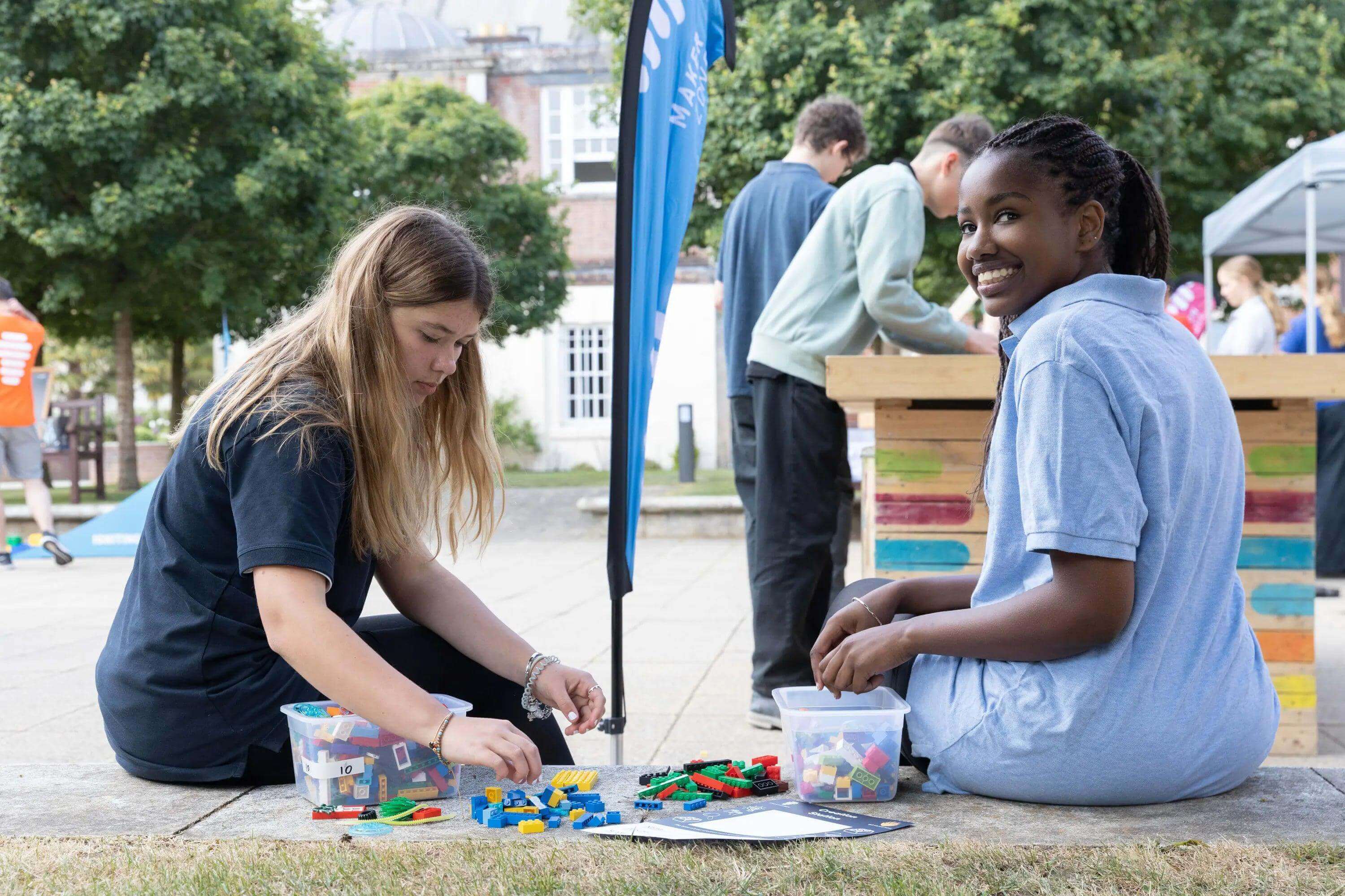 Two students engaged in creativity, playing with colorful building blocks outdoors at the Bryanston Education Summit.